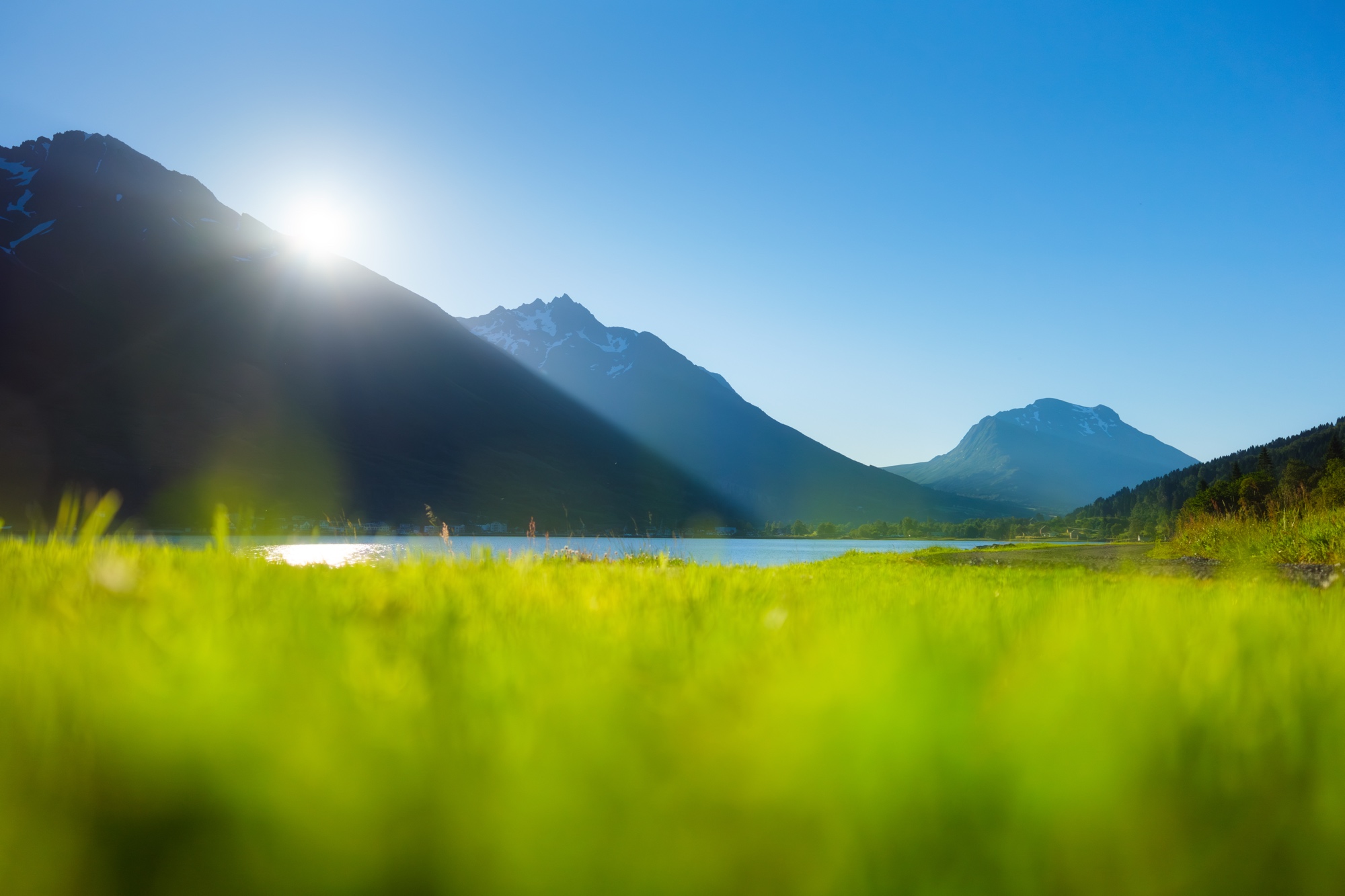 Sonnenaufgang über einem See mit Bergen und grüner Wiese